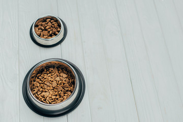 metal bowls with pet food on white wooden surface