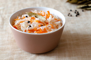 Homemade sauerkraut with carrots, sunflower oil, whole-grain yeast-free bread and black pepper in a bowl on a linen napkin. Side view.