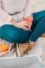 Woman with glass of rose wine is sitting on the beach, having autumn picnic herself.