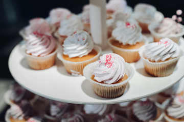 Selective focus of cute delicious cupcakes served on plate. Closeup of yummy desserts with cream staying on table. Concept of wedding candy bar, desserts and confectionery.