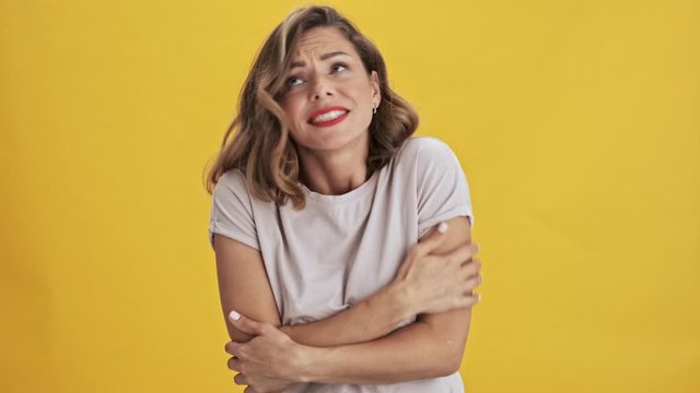 Beautiful young woman with red lips holding hands folded and shows freezing over yellow background isolated                                                                          
