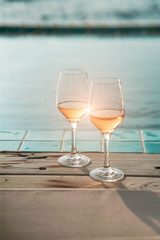 Two glasses of wine  on the edge of infinity swimming pool with panoramic views of the sea at sunset. Drink, celebrate, vacation and summer concept.