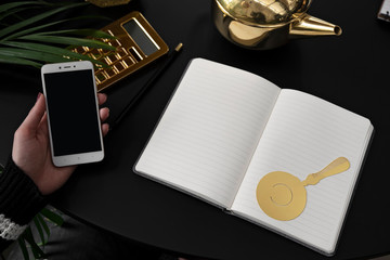 Notebook with mock up and gold tab on a black background on office desk. Smartphone with empty...