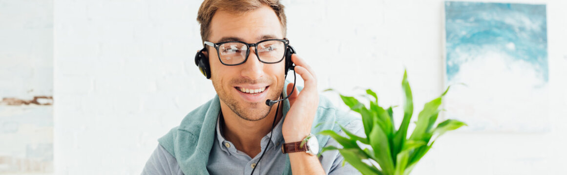 Smiling call center operator talking on headset, panoramic shot