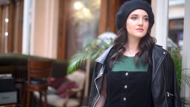 Beautiful young woman with long brunette hair in black beret over street cafe