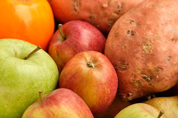 Colorful background with healthy fruits and vegetables like apples, kaki and sweet potatoes lying close together.