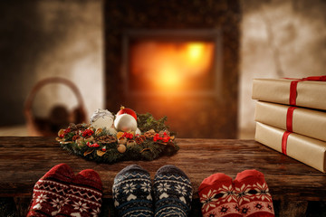 Woolen christmas socks and woman legs on wooden table. Free space for your decoration.Fireplace in home interior with warm orange light of fire.Copy space and winter cold night.Xmas time and gifts.