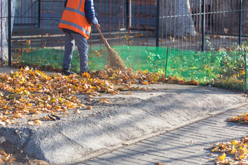 A cleaning lady cleans the dead side of the maple leaves from the sidewalk.