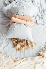 Fototapeta na wymiar top view of woman covering face with pillow in bedroom