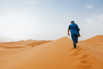 Man with classic berber clothes on walking by the desert dunes alone.