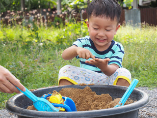 Asian cute child boy laughing with happy smiling face while playing sand with dad as natural meadow background with happy family time.