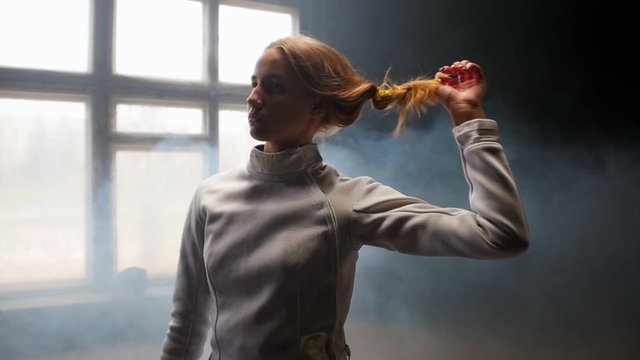 A young woman fencer she lets her hair down and shakes her head down and back