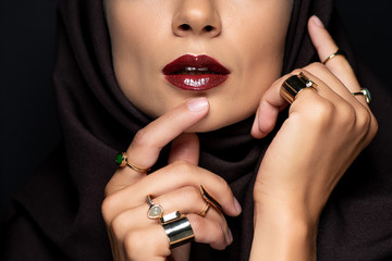 cropped view of beautiful Muslim woman in hijab with makeup in golden rings isolated on black