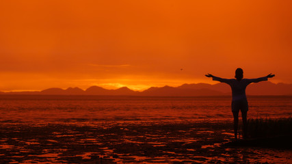 Fototapeta premium Girl in front of amazing orange sunset open arms.