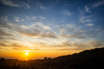 Obraz premium Sunset sky. Sea, mountains. Black outlines of the city and mountains.