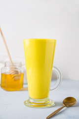 Glass of ayurvedic golden turmeric latte milk with honey and curcuma on white. Natural detox beverage. Close up. Vertical shot. Trendy Asian healthy drink for immunity with spices for vegans.