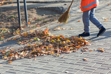 A cleaning lady cleans the dead side of the maple leaves from the sidewalk.
