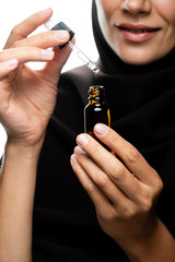 partial view of young Muslim woman in hijab holding dropper an bottle with serum isolated on white