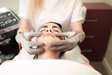 Doctor cosmetologist does facial massage to the patient with electric gloves