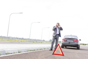 Stressed businessman talking on smartphone and asking help for his broken car