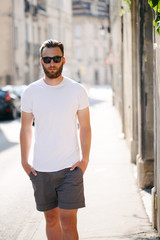 Hipster handsome male model with beard wearing white blank t-shirt with space for your logo or design in casual urban style