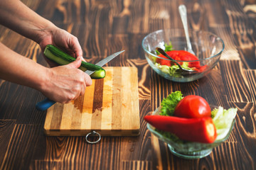 Young woman is cutting cucumber on cutting board for salad