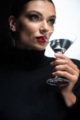 portrait of beautiful elegant woman with red lips drinking martini isolated on white and black