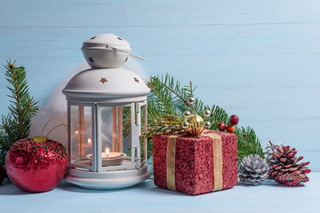 Cozy chrstmas holiday composition. White lantern with burning cadle, gift box and christmas decorations on the blue paint wooden background. Copy space © stsvirkun