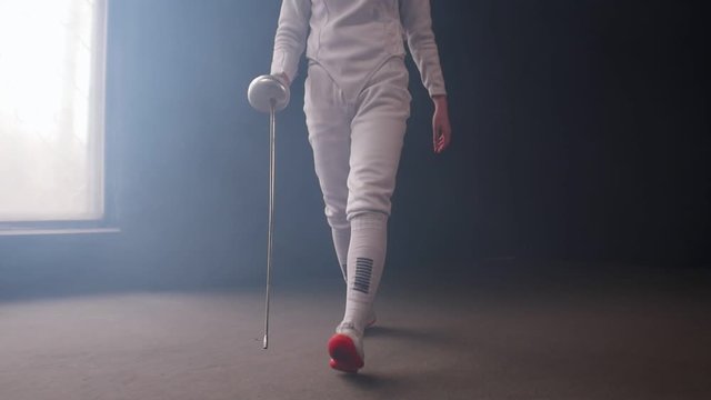 A young woman fencer with loose hair in white costume performing basic attack movements