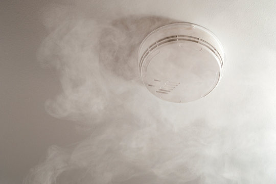 Fire alarm system and home security conceptual idea with smoke rising to the ceiling and activating the generic smoke detector isolated on white with copy space