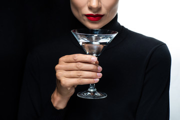 cropped view of beautiful woman with red lips holding martini isolated on white and black