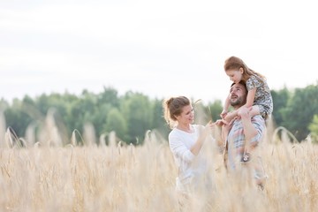 Father carrying his daughter on shoulders while walking with his wife in field © MDBPIXS