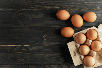 Chicken eggs in carton box on wooden background, space for text