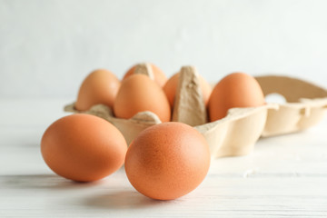 Chicken eggs in carton box on wooden table against white background
