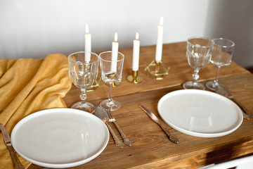 Table is served for a Christmas dinner in the living room, close-up view, table setting with a golden tablecloth, white plates, forks, knives, glasses for wine, candles in gold candlesticks, Christmas