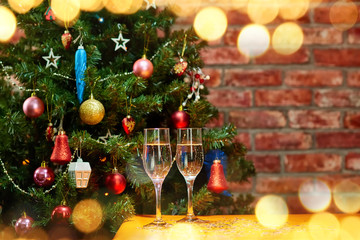 Fototapeta na wymiar Two glasses of champagne on the background of a beautifully decorated balls, garlands, stars Christmas tree. Around the glow of rays and bokeh lights
