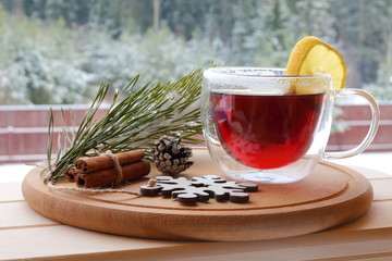 The glass mug of hot tea on the winter forest background. 