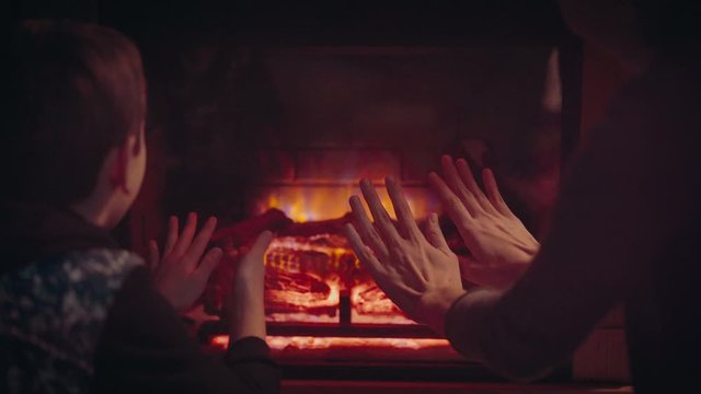 Mom and son warm their hands by the fireplace.