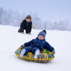 The laughing cute toddler, 3 years old, is sliding down the hill in winter.