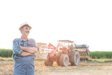 Confident senior farmer standing with arms crossed in field