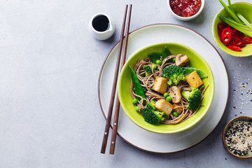 Soba noodles with vegetables and fried tofu in a bowl. Grey background. Copy space. Top view.