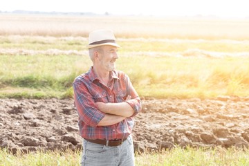 Senior farmer standing with arms crossed in field