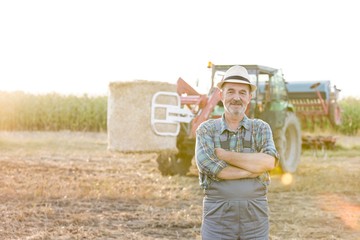 Confident senior farmer standing with arms crossed in field