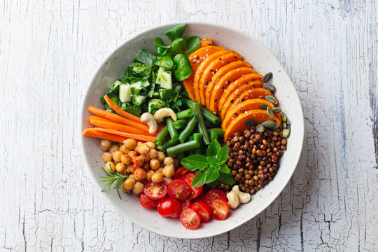 Healthy vegetarian salad. Lentil, chickpea, carrot, pumpkin, tomatoes, cucumber. Wooden background. Top view.