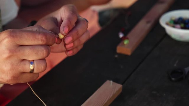 Close-up of female hands stringing beads on a thread, making a jewelry bracelet