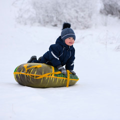 Fototapeta na wymiar The smiling cute toddler, 3 years old, with his inflatable round sleigh is outdoors in winter.