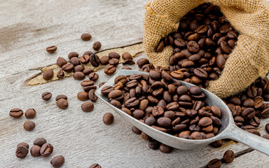 Dark roasted coffee beans with scoop on wooden background