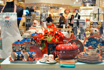 Moscow, Russia, November 2019: tableware shop Window: a set of bright plates, cups in the Mexican style, the inscription "La vida", apron, tureen in the form of pumpkin. Buyers on a blurred background