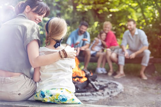 Rear view of mother sitting with arm around daughter while camping at park