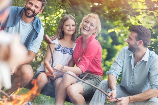 Tilt shot of happy family with male friend roasting sausages over campfire at park